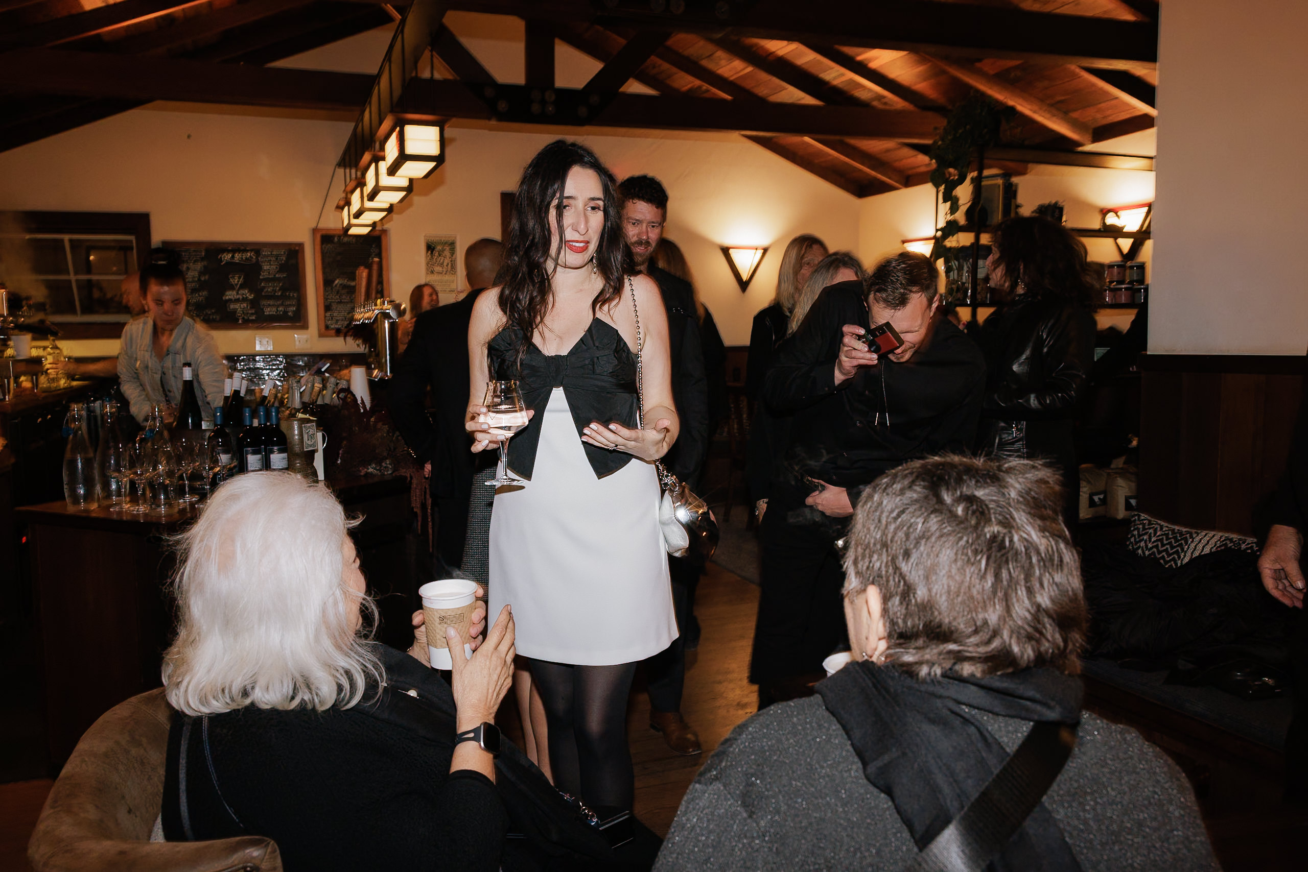 Elegant woman in black and white enjoying a drink at a warmly lit Mendocino wedding venue.