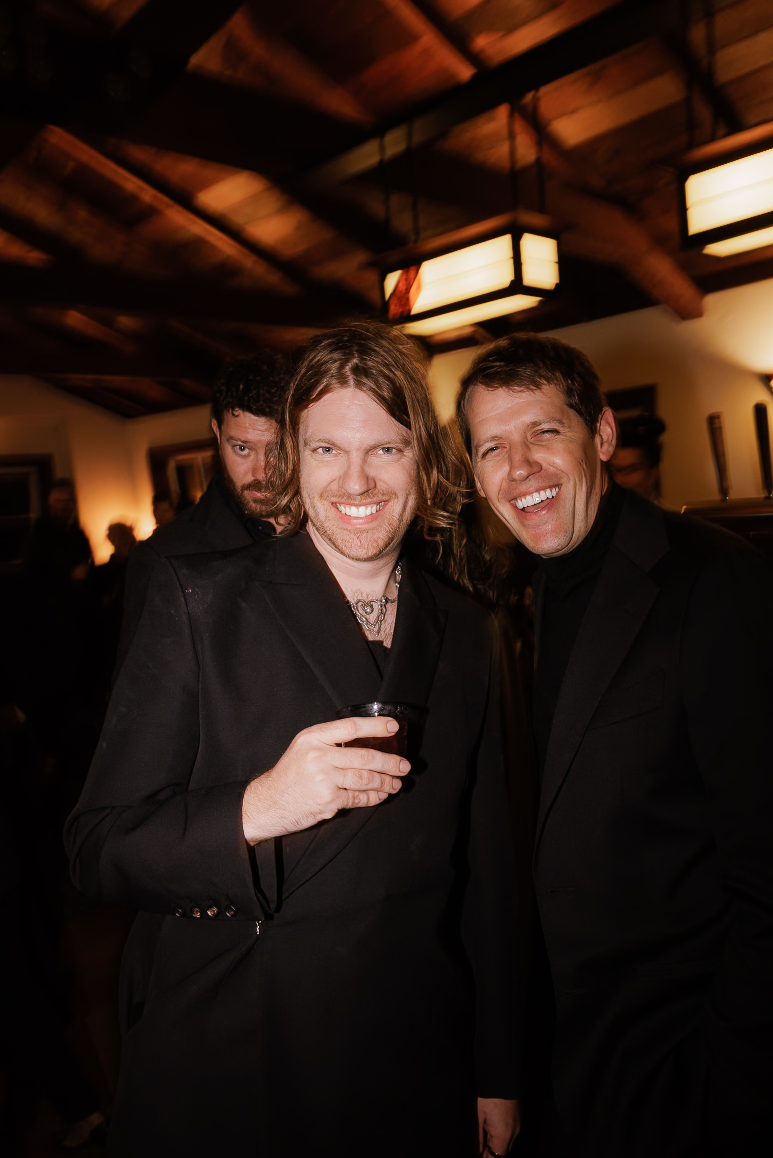 Elegant Mendocino wedding: Two grooms in black attire, warmly lit setting, intimate celebration.