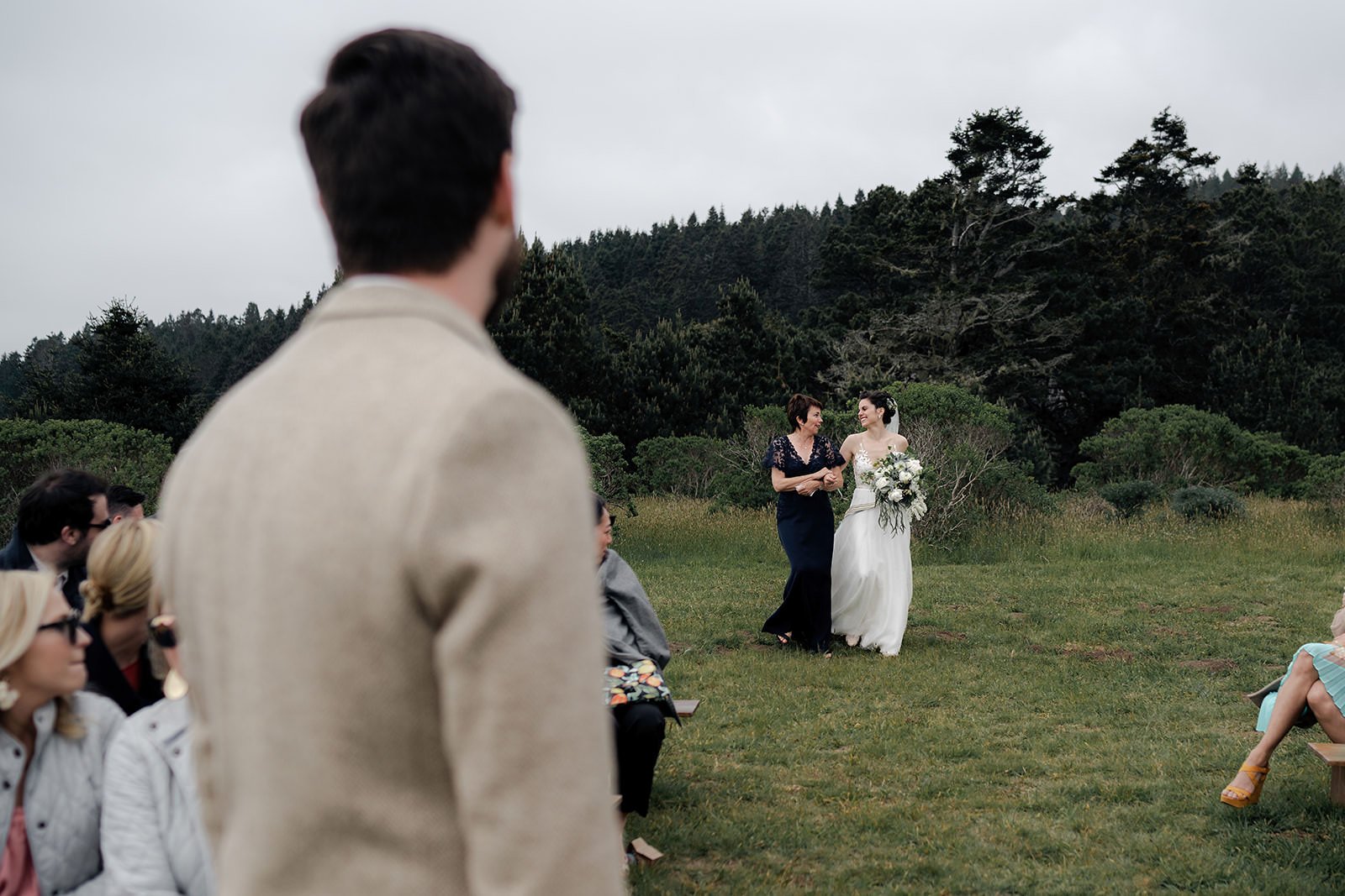 Bride in white with older woman at Cuffey Cove; enchanting outdoor wedding aisle shot.
