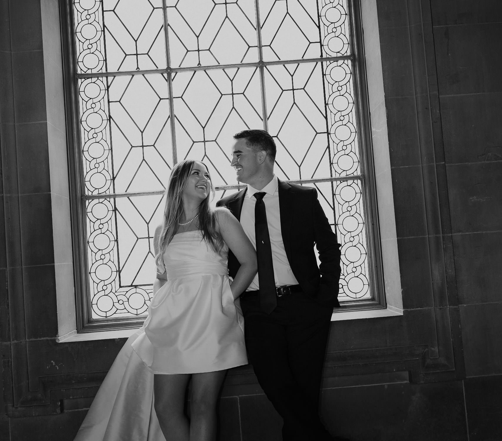 Elegant Couple in Black & White: Timeless Wedding Photography at Ornate Window.
