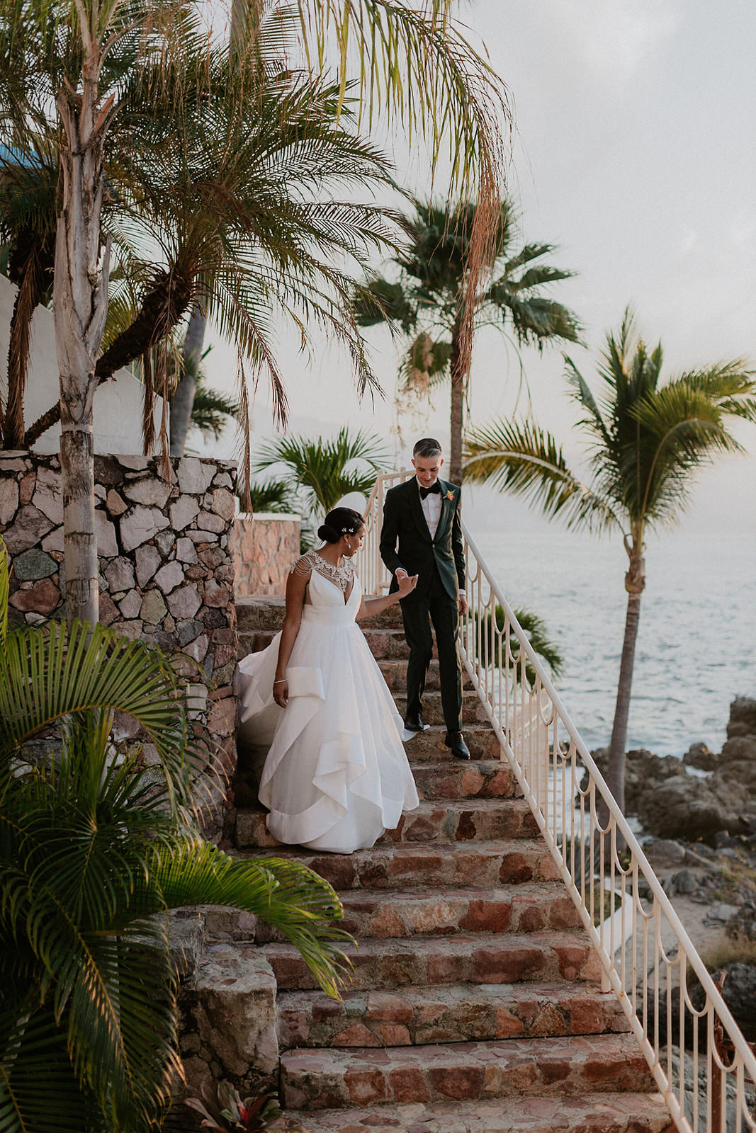 Elegant Wedding in Puerto Vallarta: Bride and Groom on Palm-Lined Steps by the Ocean.