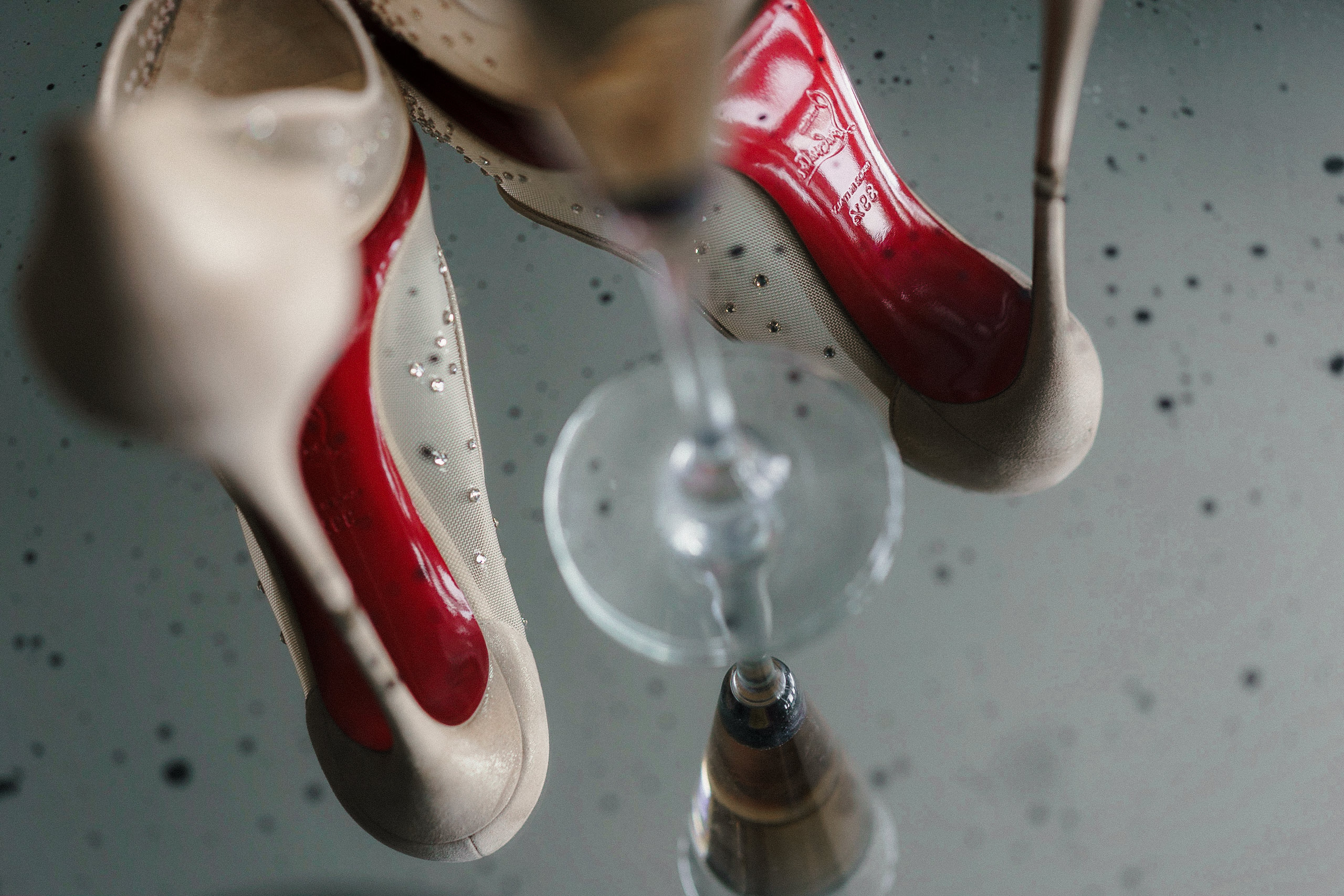 Elegant beige heels with iconic red soles reflect on a glossy surface, paired with a champagne flute.