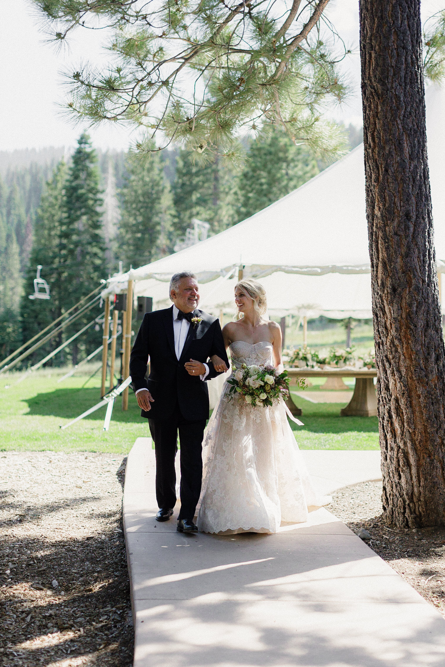 Luxury wedding photography at The Ritz-Carlton, Lake Tahoe: Bride and groom stroll under sunlit forest canopy.
