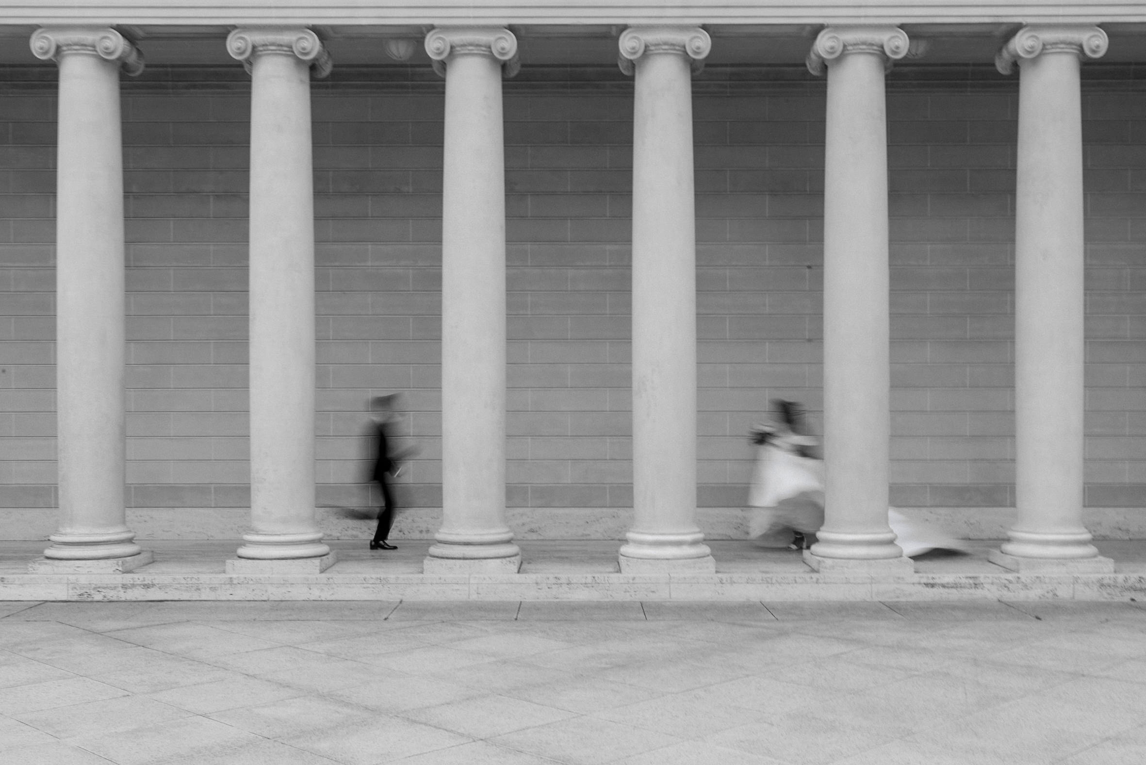 Elegant black and white wedding photo: blurred couple, classical columns, stone wall background.
