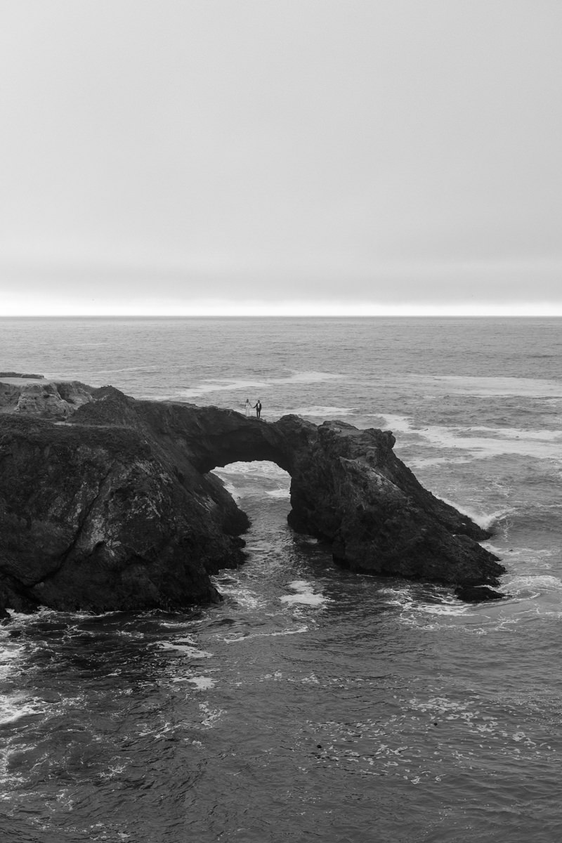 Stunning Black & White Coastal Arch Wedding Portrait with Dramatic Sky.