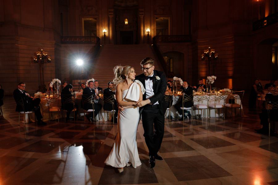 Elegant Ballroom Wedding Dance | Bride in White Gown, Groom in Black Tuxedo, Smiling Guests.