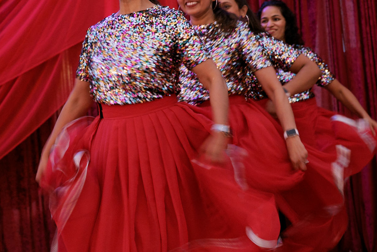 Elegant women in sequined tops and red skirts dance amid luxurious drapery at a vibrant celebration.
