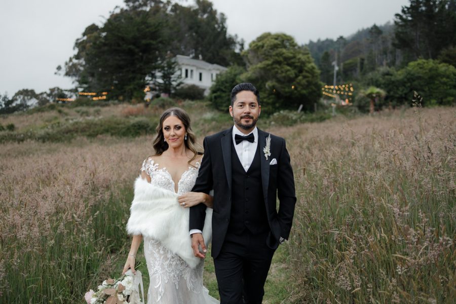 Elegant Bride & Groom: Lace Gown, Shawl, Tuxedo in Scenic Field with Trees & Illuminated House.