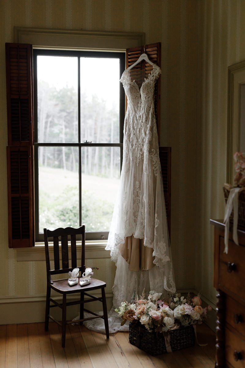 Elegant Lace Wedding Dress by Window with Silver Heels and Pastel Florals - Serene Bridal Atmosphere.
