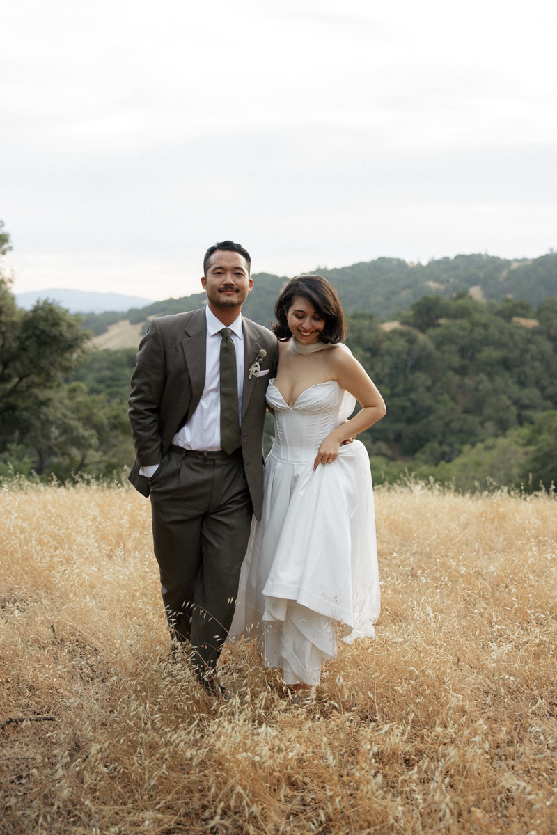 Elegant Couple in Scenic Hills: Brown Suit, White Dress, Holding Hands - Professional Wedding Photography.
