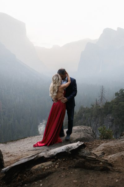 Engagement Session on Rocky Cliff: Couple Embraces Amidst Serene Mountain Scenery.